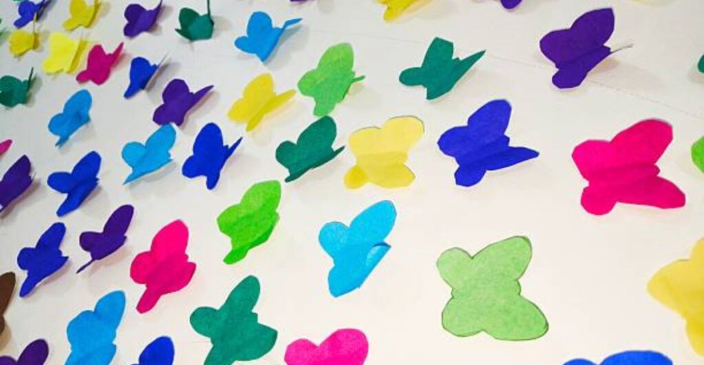 Colorful paper butterfly wall art with handmade pastel wings and floral decorations.