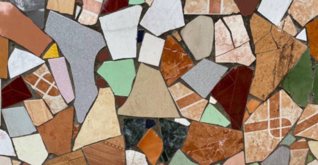 Broken ceramic tiles creatively arranged in a colorful courtyard pathway surrounded by lush green plants.