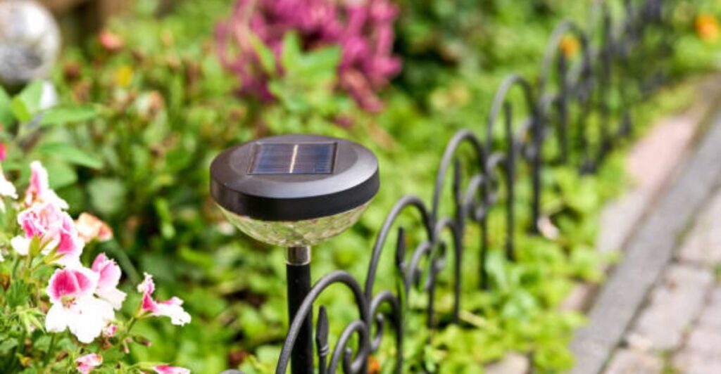 Rustic solar lanterns lining a curved garden pathway bordered with colorful flowers in a small backyard garden.