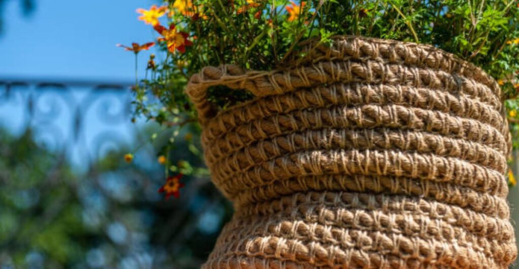 Rope-wrapped plant pot with natural jute texture placed on a modern wooden shelf in a bright living room.