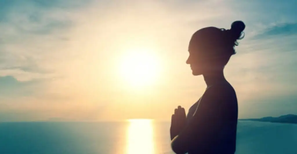 Person praying with folded hands at sunrise, expressing gratitude to begin the morning with faith and thankfulness.