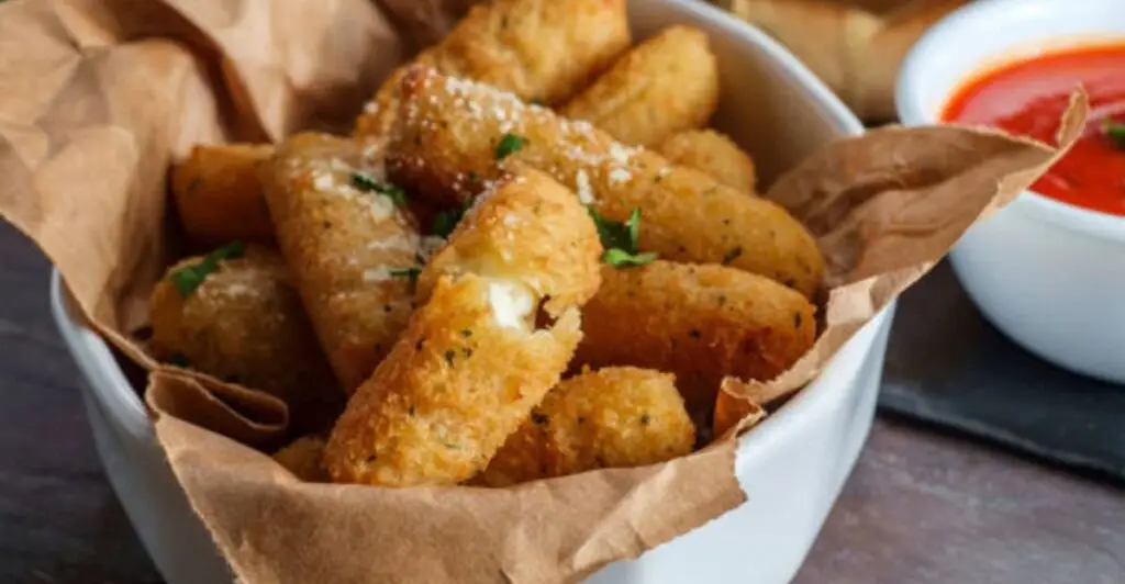 Freshly cooked mozzarella sticks arranged on a serving plate with dipping sauce